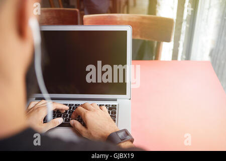 Junge bärtige Geschäftsmann tragen schwarze Tshirt arbeiten Laptop Urban Cafe.Man sitzen Holztisch Kopfhörer mit Notebook leer Screen.Coworking Prozess Business Startup.Blurred Hintergrund Stockfoto