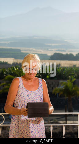 Senior Expat-Frau auf Balkon mit iPad Tablet-Gerät mit den Teide im Hintergrund, Teneriffa, Kanarische Inseln, Spanien Stockfoto