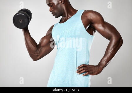 Schuss von afrikanischem jungen muskulösen Mann, der schwere Hantelübungen für Bizeps macht. Fitness männliches Modell mit Kurzhanteln auf gr Stockfoto