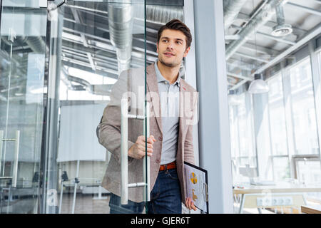 Hübscher junger Geschäftsmann mit Zwischenablage in die Tür im Büro Stockfoto