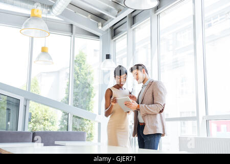 Lächelnde junge Geschäftsmann und Busineesswoman stehen und mit Tablette zusammen im Büro Stockfoto