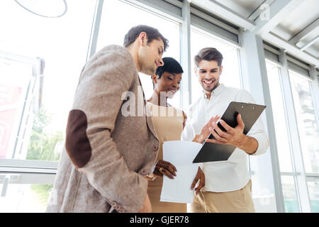Drei glückliche junge Geschäftsleute sprechen und uns über Dokumente zusammen im Büro Stockfoto