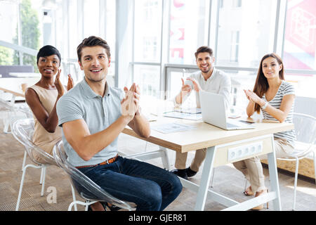 Gruppe von fröhlichen jungen Geschäftsleuten auf Präsentation im Büro sitzen und klatschten Stockfoto