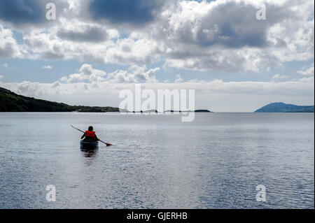 Eine weibliche Kajakfahrer Paddel vom Meer entfernt auf einem ruhigen Meer in West Cork, Irland. Stockfoto