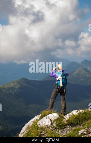 Frau am Gipfel des Mount Benediktenwand fotografieren auf das Bergpanorama mit einem Smartphone, Bayern, Deutschland Stockfoto