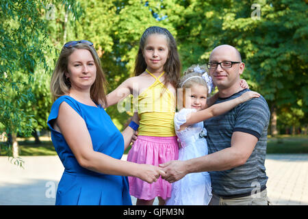 glückliche Familie posiert auf im Freien, eine Gruppe von vier Personen Porträt im Stadtpark, Sommersaison, Kind und Elternteil Stockfoto