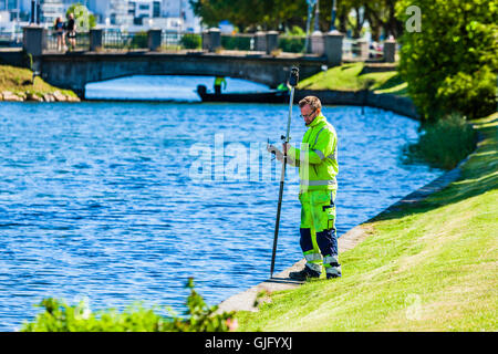 Kalmar, Schweden - 10. August 2016: Männlicher Arbeitnehmer tun, irgendeine Art von Messung durch den Kanal mit einem Instrument auf einen Stick und GPS. Stockfoto