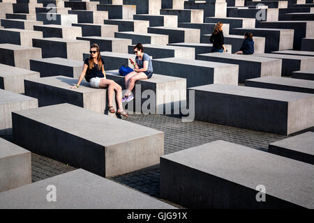 Touristen sitzen auf die Betonsteine von das Holocaust-Mahnmal für die ermordeten Juden Europas, Berlin, Deutschland. Stockfoto