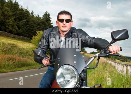 Motorradfahrer Motorradfahrer sitzt auf einem Motorrad in Landschaft mit blauem Himmel Leder Jacke Sonnenbrille Retro-Motorrad Stockfoto