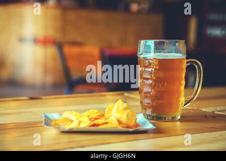 Ein frisches Glas kaltes helles Bier und Chips auf der hölzernen Tresen im Pub mit Freiraum für Ihren Text. Schöne zurück Stockfoto