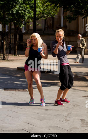 Dundee, Tayside, Scotland, UK. 16. August 2016: UK Wetter. August Hitzewelle pauschal über Tayside heute mit der maximalen Temperatur 27 ° C. Obwohl die Schulen in Schottland wieder geöffnet haben andere genießen die herrlichste warme Sonnenstrahlen im Zentrum Stadt. Zwei Fit athletische Frauen tragen Sportswear halten ihre Tassen Kaffee anhalten für ein Foto entlang Dundee High Street. Bildnachweis: Dundee Photographics / Alamy Live News Stockfoto