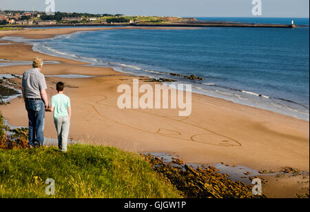 Spittal, Berwick nach Tweed, Northumberland, UK. 16. August 2016. Mike Greener und Enkel Lewis Waddell (10) Blick hinunter auf den größten Lachs der Tweed hat je gesehen.  Sean Corcoran, "Der Kunst Hand" von Bunmahon, Co. Waterford, Irland schafft massive Sandart Zeichnungen mit einer Harke, seinen ersten internationalen Einsatz als ein Sand-Künstler Spittal Seaside Festival in Northumberland.  Seans letzte Arbeit war ein Lachs geschaffen, um erinnern und feiern die Lachs Fischer des Flusses Tweed, seine 400 Fuß lange Lachs war auf dem Gelände des Huds Head Fischerei. Stockfoto