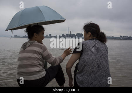 Dandong, Liaoning, China. 24. Juli 2016. Zwei chinesische Frauen sitzt am Ufer Flusses Yalu-Fluss und sprechen, ist das Gegenteil des Flusses Sinuiju, Nordkorea. In Dandong, Provinz Liaoning. China und Nordkorea über 1.420-km-Grenze, den Yalu und Tumen Flüsse, wie die natürliche Grenze trennen beider Länder. China und Nordkorea waren einst berühmte intimes als ' Lippen und Zähne ''. Wie Kim Jong-Un als Supremo der Volksdemokratischen Republik Korea und die unklaren Bomben getestet wurden, trat ihre Beziehungen eine Phase der angespannt. Aber vor kurzem die Entscheidung o Stockfoto