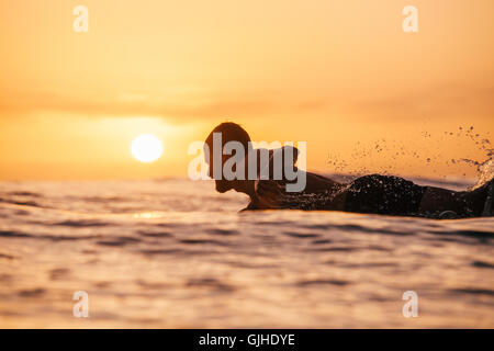 Nahaufnahme eines lächelnden Surfers, der bei Sonnenuntergang in San Diego, Kalifornien, USA, paddelt, um eine Welle zu beobachten Stockfoto