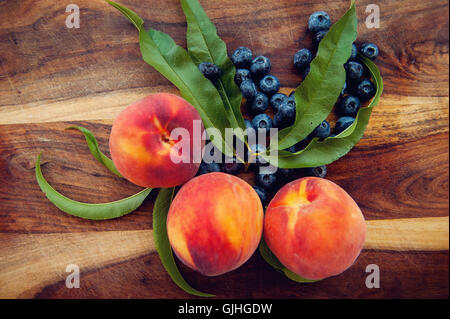 Pfirsiche und Heidelbeeren auf Schneidbrett aus Holz Stockfoto