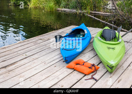 Zwei bunten Kajaks mit Fanggeräten und Schwimmweste liegen auf einem Holz- Dock an einem See. Stockfoto