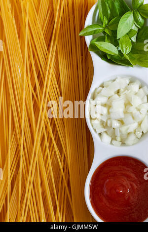 Basilikum, in Scheiben geschnittenen Zwiebeln und Tomatenmark in weiße Schüssel mit rohen Spaghetti verstreut. Konzept-Bild für italienische Küche. Nach oben Stockfoto
