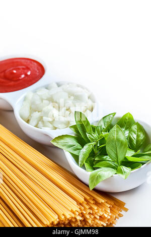 Basilikum, in Scheiben geschnittene Zwiebeln und Tomatenmark in weiße Schüssel mit rohen Spaghetti auf weißem Hintergrund. Textfreiraum Stockfoto