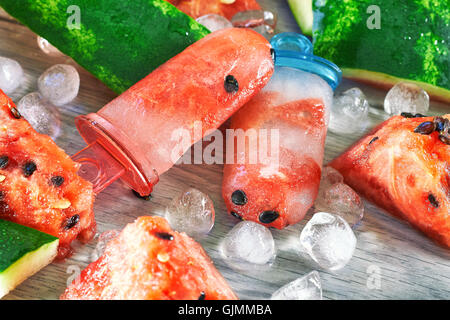 Gefrorene Wassermelone Eis am Stiel mit Eiswürfeln und Wassermelone Scheiben auf grauem Hintergrund aus Holz. Konzept-Bild für Sommer-Erfrischung Stockfoto