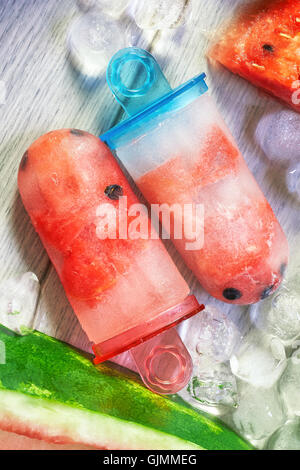 Gefrorene Wassermelone Eis am Stiel mit Eiswürfeln und Wassermelone Scheiben auf grauem Hintergrund aus Holz. Konzept-Bild für Sommer-Erfrischung Stockfoto
