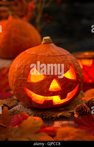 Brennen von Jack O'Lantern auf einem rustikalen Tisch mit herbstlichen Dekorationen, beleuchtet dunkel. Stockfoto