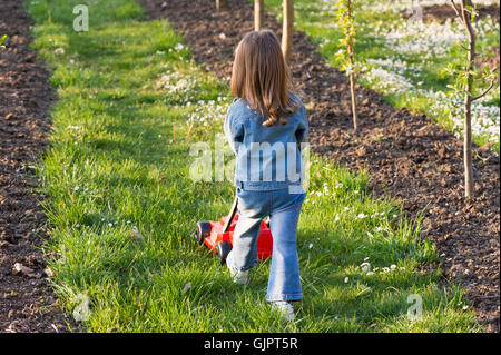 Niedliche Mädchen spielen mit einem Rasenmäher im Garten Stockfoto