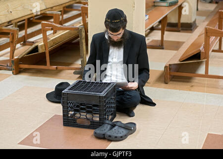 Ein religiösen jüdischer Mann sitzt auf dem Boden auf Tisha B'Av, beten ein Tag der Trauer auf dem hebräischen Kalender. Brooklyn, New York. Stockfoto