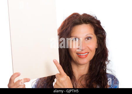 Happy Reife Frau mit arabischen und nahöstlichen somatische Merkmale und gefärbt mit Henna Haare lächelt ihr Finger auf leeren weißen Schild, den sie im Hochformat hält Stockfoto