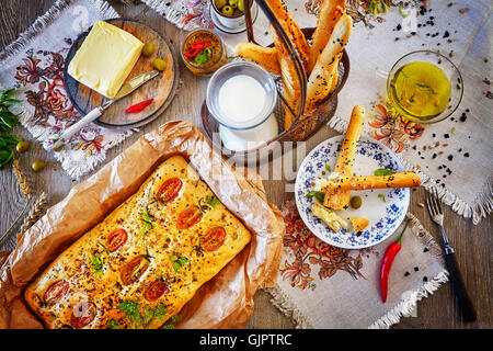 Traditionelle Focaccia in Papier und Brot backen klebt, rustikale Einrichtung auf einem Holztisch von oben. Stockfoto