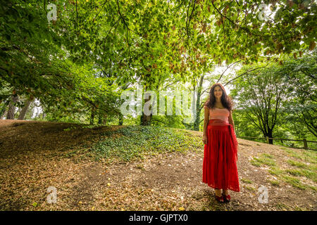 Reife Frau gekleidet in Zigeuner Kleid mit roten Rock und T-shirt aus Baumwolle mit Bateau-Ausschnitt im öffentlichen Park mit Boden fallenden Laub Stockfoto