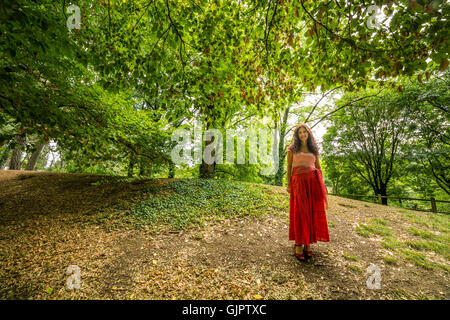 Reife Frau gekleidet in Zigeuner Kleid mit roten Rock und T-shirt aus Baumwolle mit Bateau-Ausschnitt im öffentlichen Park mit Boden fallenden Laub Stockfoto