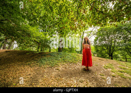 Reife Frau gekleidet in Zigeuner Kleid mit roten Rock und T-shirt aus Baumwolle mit Bateau-Ausschnitt im öffentlichen Park mit Boden fallenden Laub Stockfoto