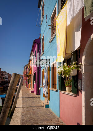 Hell gestrichene Häuser auf der Terrasse am Canalside mit Waschküche, die draußen an Wäscheleinen auf der Insel Burano hängt. Venedig, Italien. Stockfoto