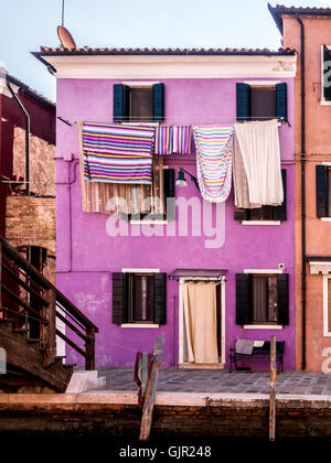 Violett gestrichenes Haus mit bunt gestreiften Wäschestüßen, die draußen an Wäscheleinen hängen. Insel Burano. Venedig, Italien Stockfoto