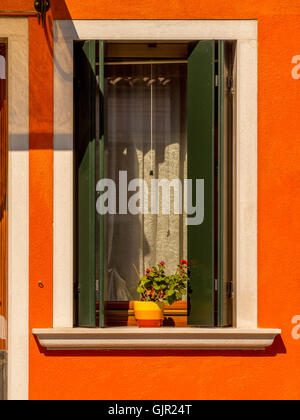 Grüne Fensterläden aus Holz und jalousien auf einem orange bemalten Haus auf der Insel Burano. Venedig, Italien. Stockfoto