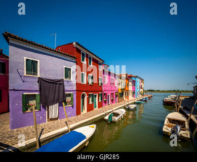 Reihe von traditionellen bunt bemalten Häusern an der Kanalseite mit Wäscheleinen, die draußen an Wäscheleinen hängen, auf der Insel Burano. Venedig Stockfoto