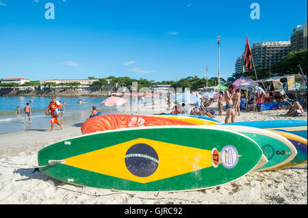 RIO DE JANEIRO - 5. April 2016: Brasilien Fahne stand Paddel Surfbrett Wartezeiten für Kunden am Strand der Copacabana. Stockfoto