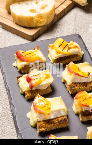 Kanapees, Vorspeise mit gegrilltem Brie und Nektarine auf einer Schiefertafel Schale vergoldet Stockfoto