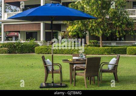 Rattan-Möbel, Tisch, Stühlen, Sonnenschirm und Outdoor-Kissen set im Garten Stockfoto