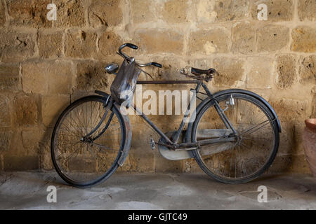 Ein altes pedal Bike lehnt sich gegen eine Mauer aus Stein. Ein Beutel hängt von den Lenkstangen Stockfoto