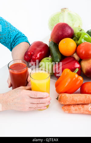 Händen der Reife Frauen setzen zwei Gläser mit roten und gelben Saft auf dem Tisch in der Nähe von Obst und Gemüse Stockfoto