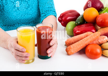 Frau legt zwei Gläser mit Orange und Tomatensaft mit Obst und Gemüse auf den Tisch Stockfoto