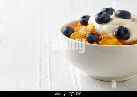 Schüssel mit Cornflakes und Blaubeeren mit Joghurt auf weißer Holztisch Stockfoto