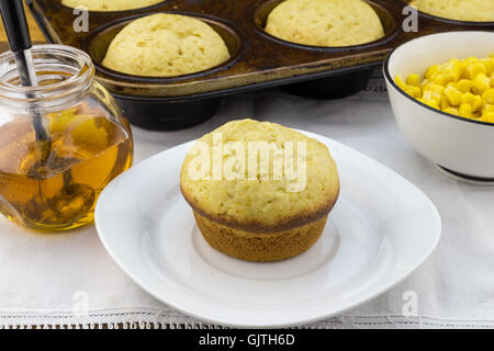 Foto von Mais Muffin in Platte mit Muffins in Pfanne, Sirup und Mais in einer Schüssel auf dem weißen Tuch Stockfoto