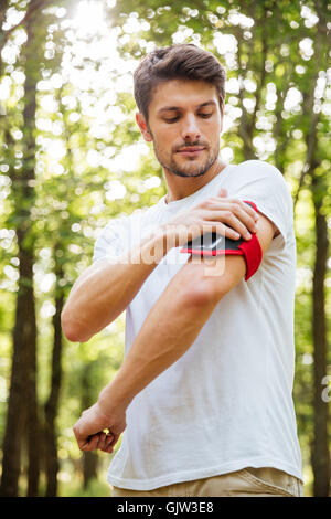 Ernste junge Sportler mit Handy in Handband Natur Stockfoto