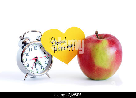 Guten Morgen Inschrift auf gelbem Papierherz zwischen Apple und Wecker Stockfoto