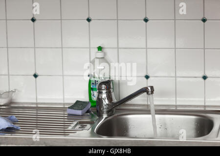 Wasser fließt aus dem Wasserhahn im Waschbecken mit Gerichten Stockfoto