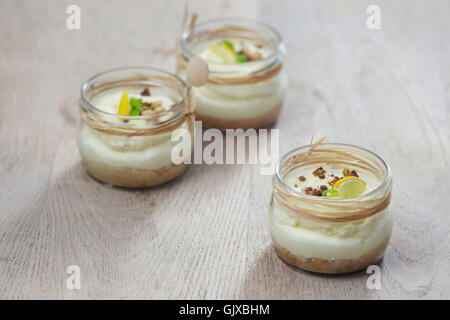 Zitronen-Mousse-Pudding mit Müsli Kruste serviert in kleinen Einweckgläser. Geringe Schärfentiefe, Gegenlicht. Stockfoto