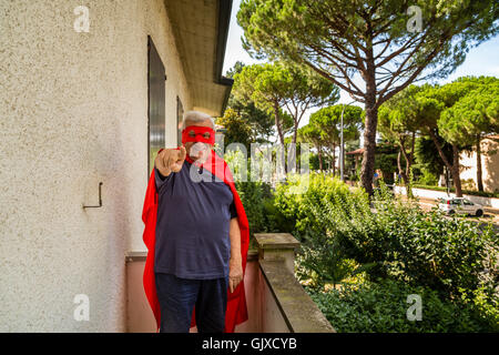 ein Alter Mann, gekleidet wie ein Superheld in Richtung Kamera mit dem Finger auf dem Balkon seines Hauses Stockfoto