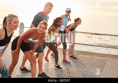 Schuss von Athleten am Start eines Marathons. Heterogene Gruppe von Menschen zusammen direkt an Strandpromenade laufen. Stockfoto